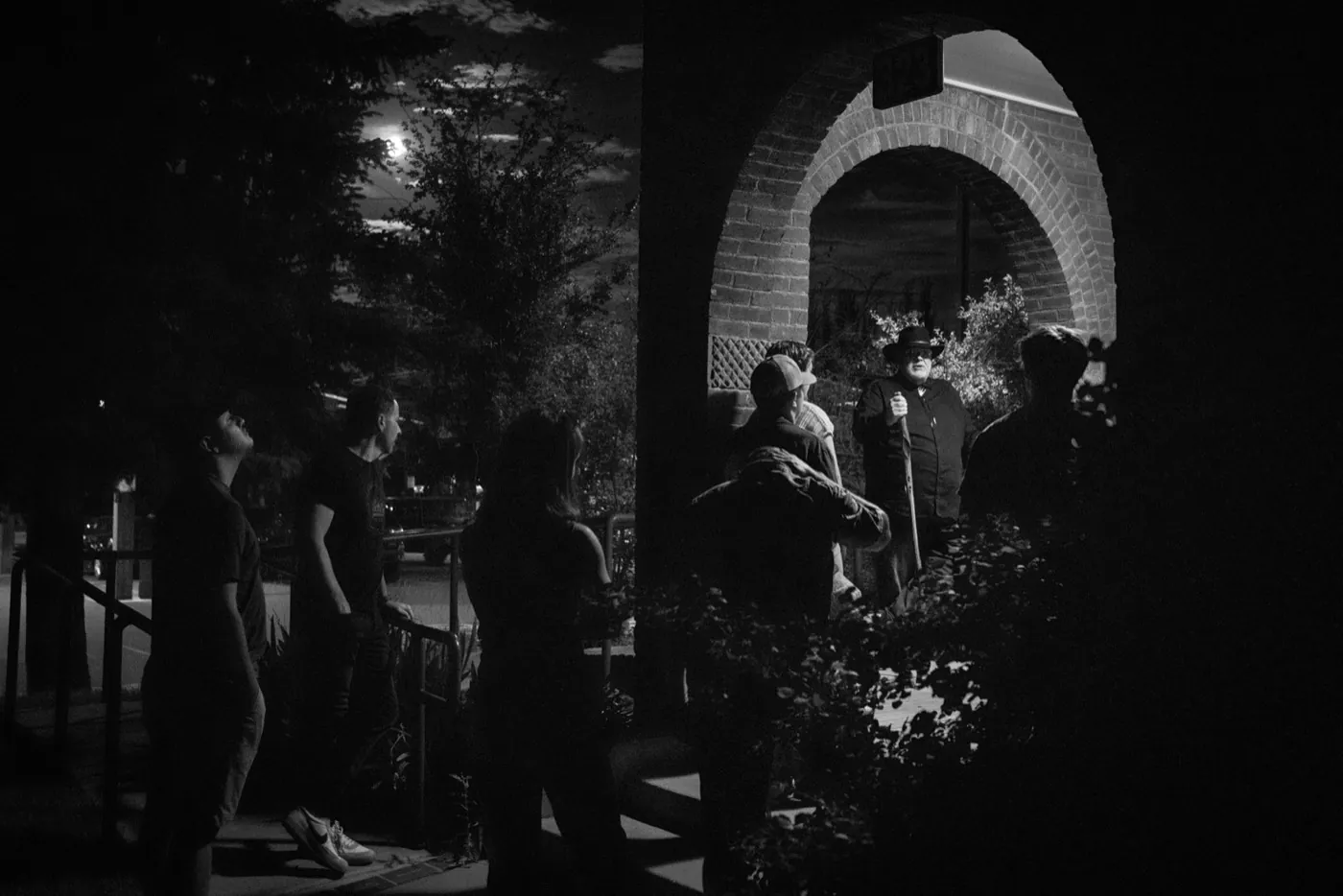 A costumed guide with a cane telling a story under a brick archway in moonlight